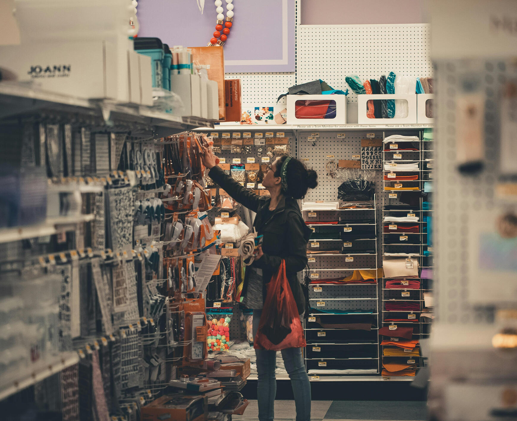 An image displaying a woman choosing a tool in an aisle She is surrounded by aisles of tools and other things that she might beneficial for her project.