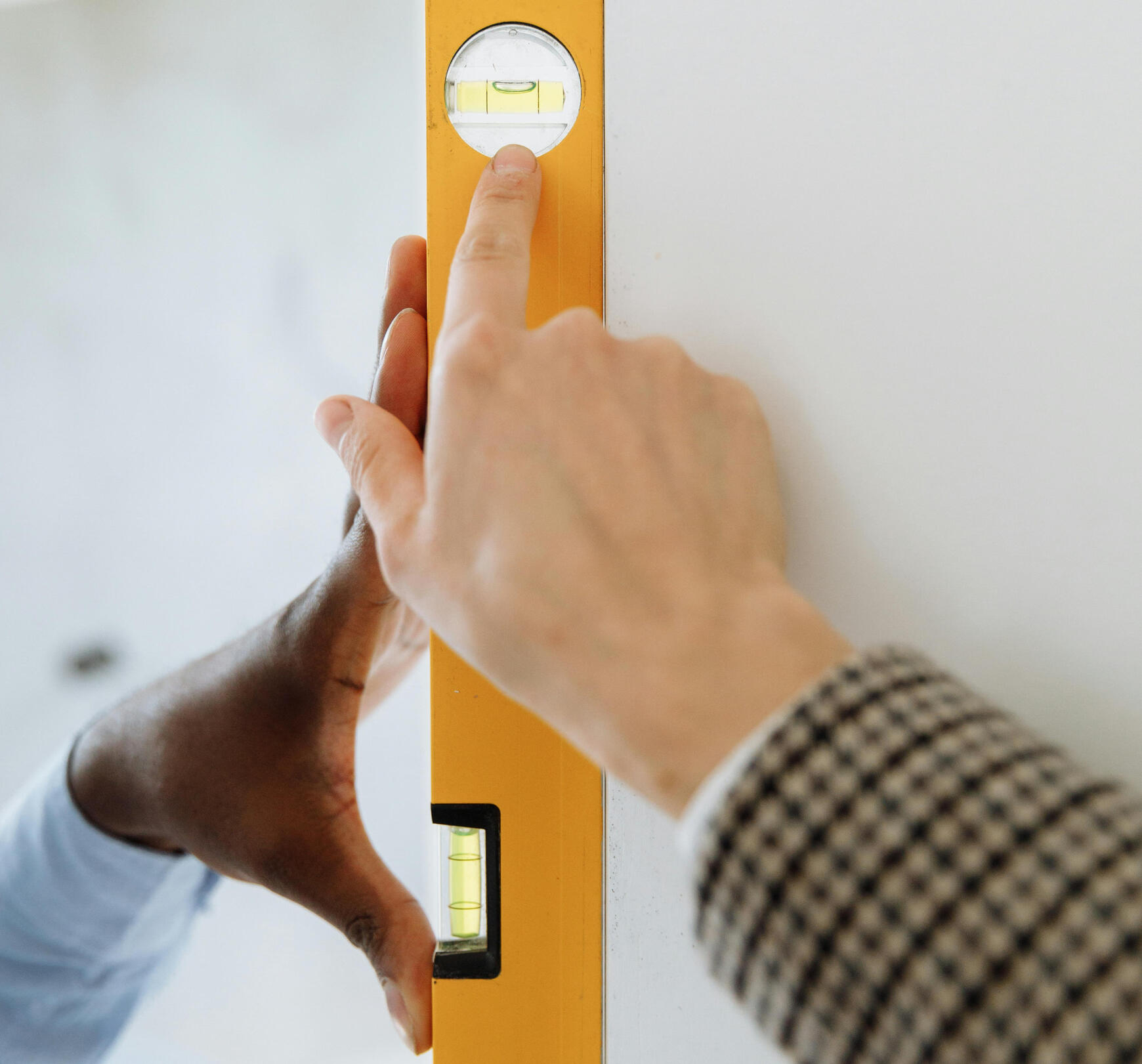 An image displaying a bubble level meter. One hand is holding the meter against the wall. Another is pointing towards the bubble.